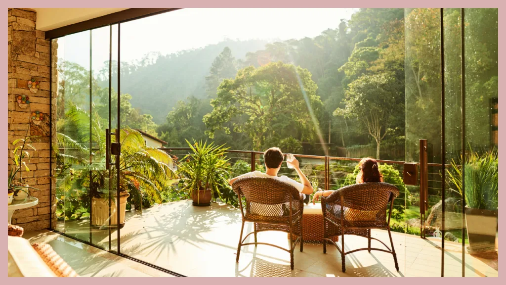 A couple relaxing on the balcony of a luxury hillside home overlooking scenic rolling hills and mature trees. The peaceful setting represents the lifestyle often associated with higher value homes and serves as a visual for understanding the difference between conforming and jumbo loans based on loan amount rather than the home's appearance or price alone.
