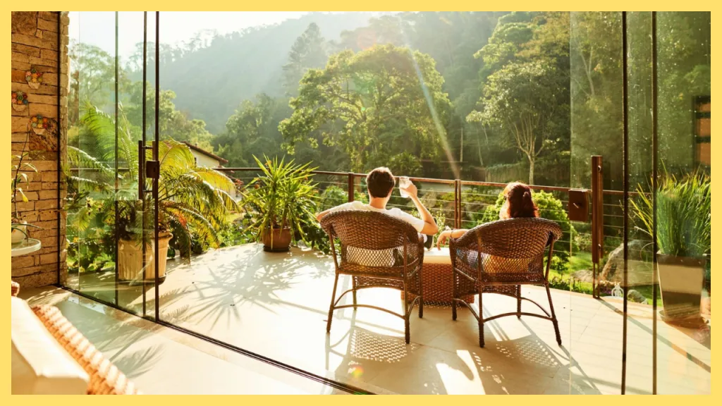 Couple relaxing on a sunlit patio overlooking lush trees and rolling hills, enjoying the peaceful outdoor lifestyle at a beautiful countryside home.