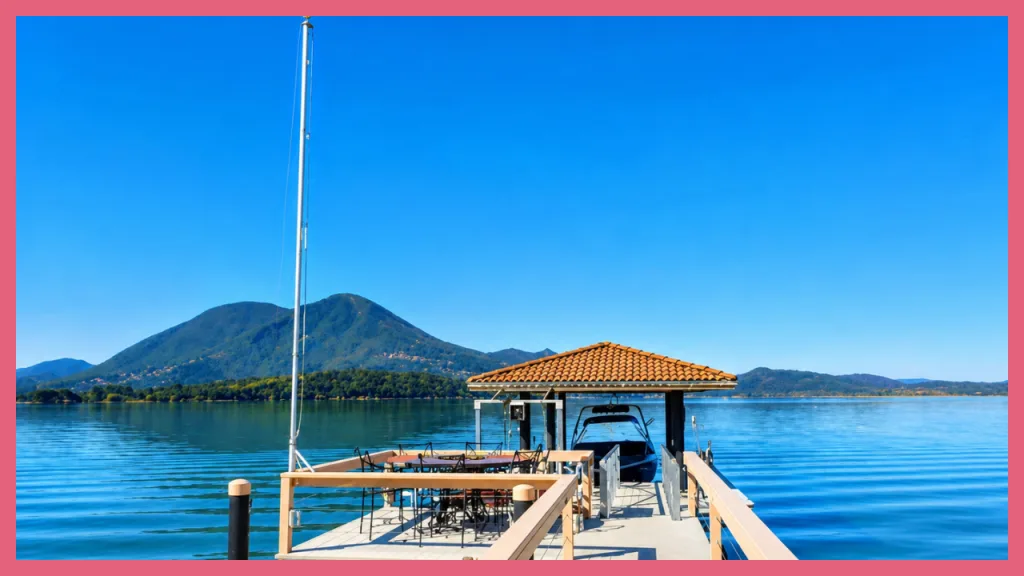 Private lakefront dock with a covered boat slip, outdoor dining area, and sailboat overlooking a calm Northern California lake surrounded by rolling mountains, illustrating a family property that was refinanced and shared across generations as part of a long term homeownership and inheritance strategy.