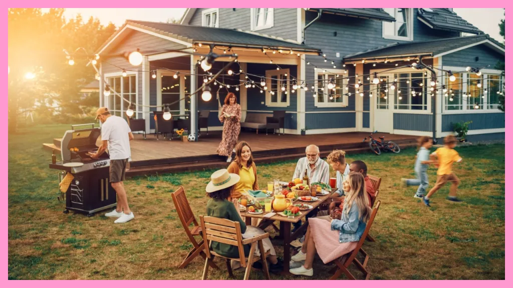 Multi generational family enjoying dinner together in the backyard of a large home, showing grandparents, parents, and children spending time together outdoors.