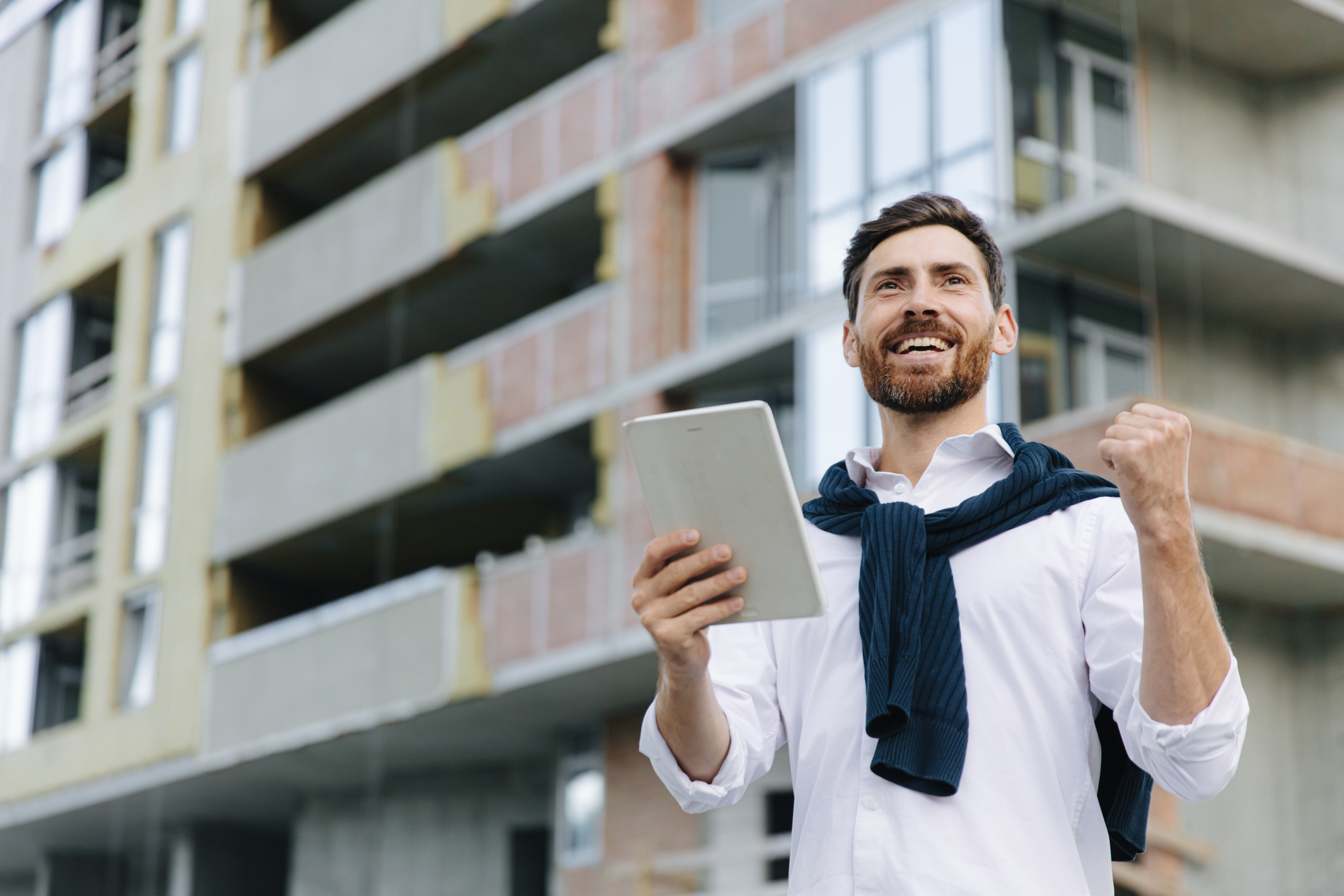 A smiling man holding a tablet outside an apartment building