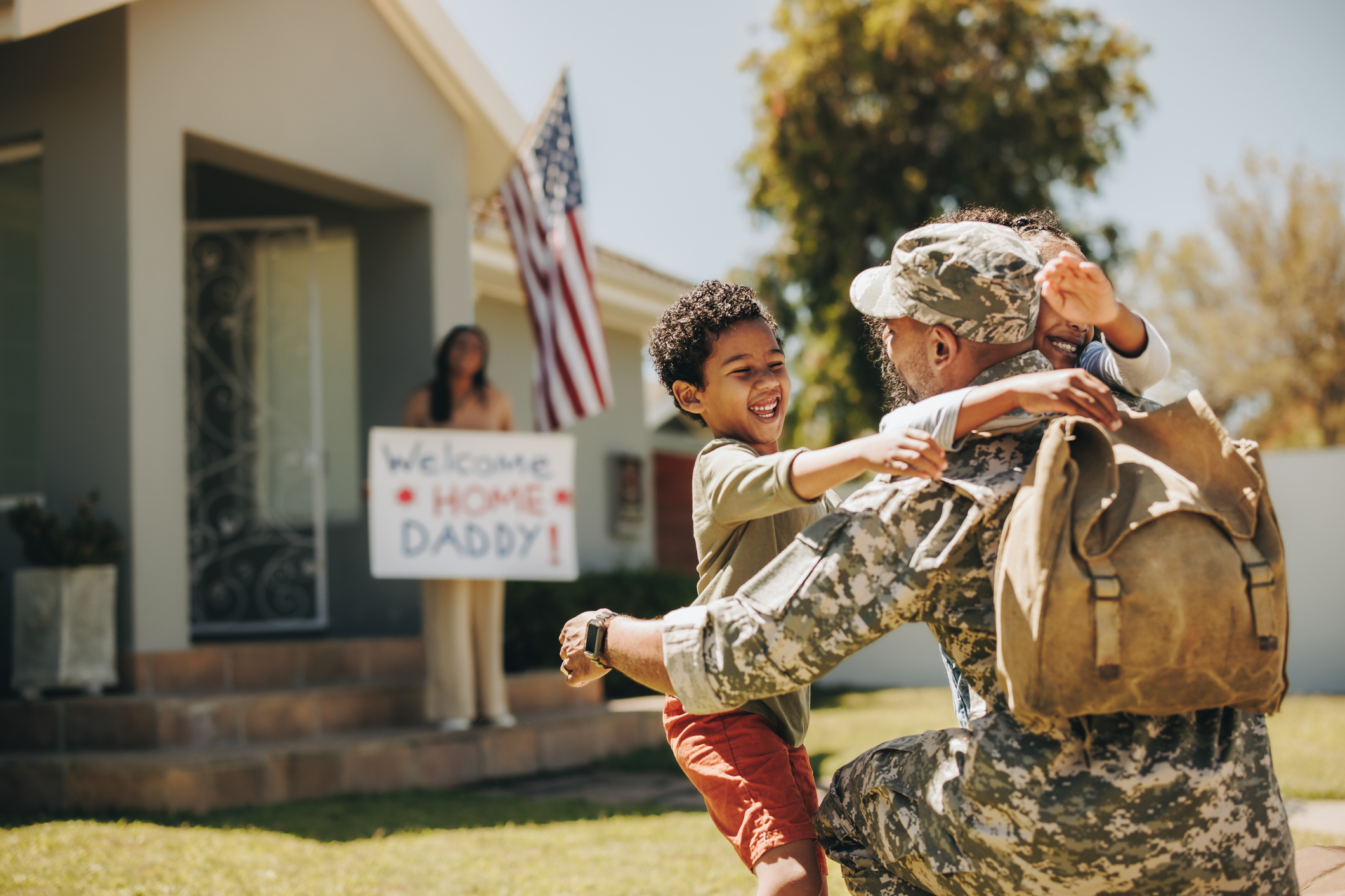 A service member embracing his children during a homecoming outside their house